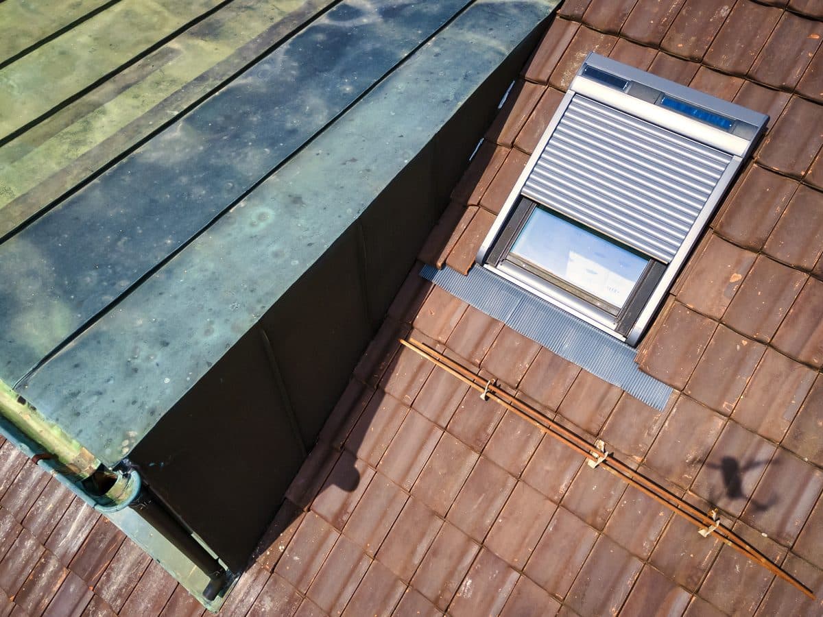Ziegeldach mit einem Dachflächenfenster, dessen Rollladen heruntergelassen ist
